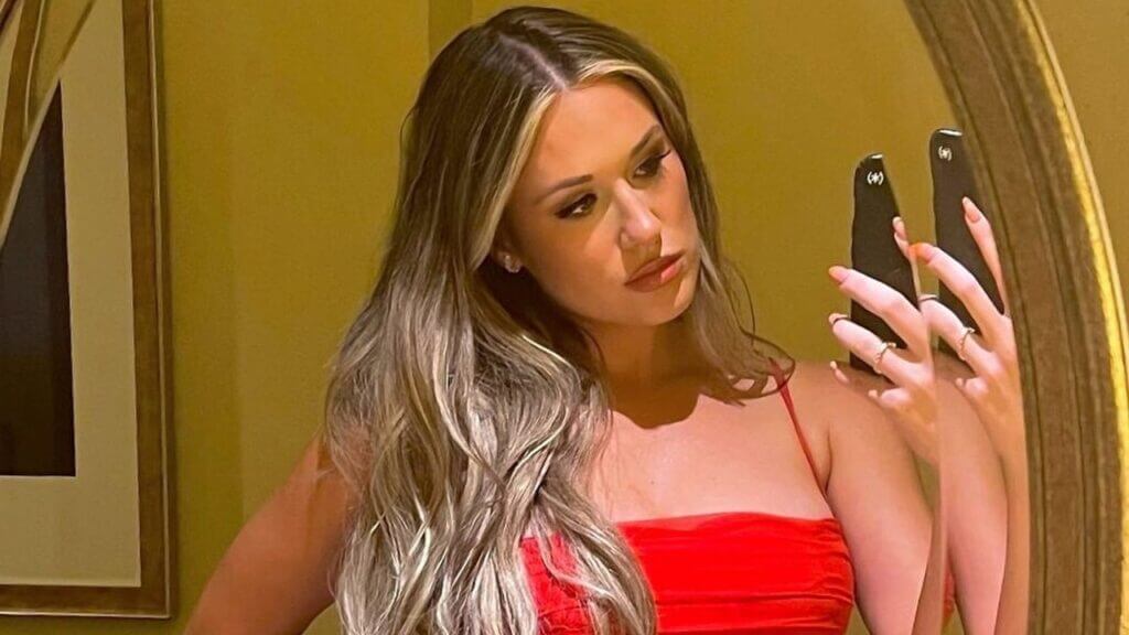 Rachel Recchia poses in red outfit while holding her phone