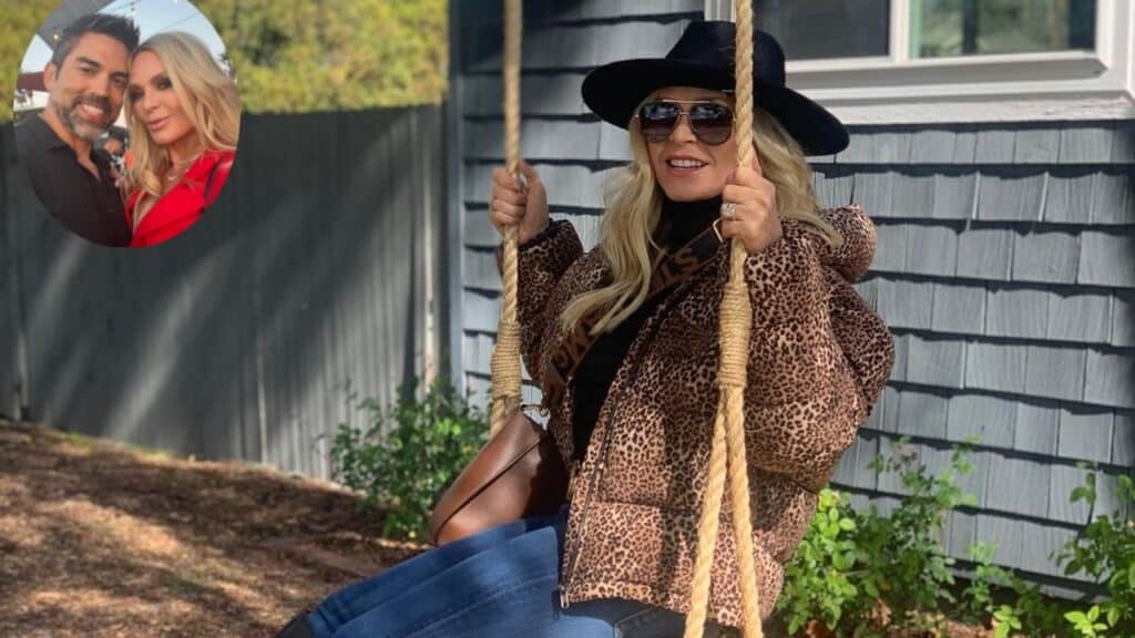Tamra Judge sits on a swing, wearing a hat, sunglasses and a brown jacket