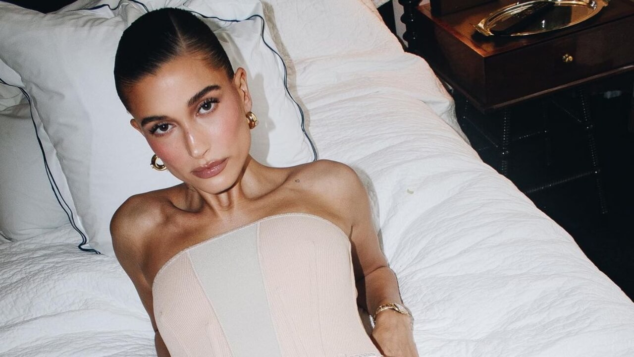Hailey Bieber in white dress lying on a bed
