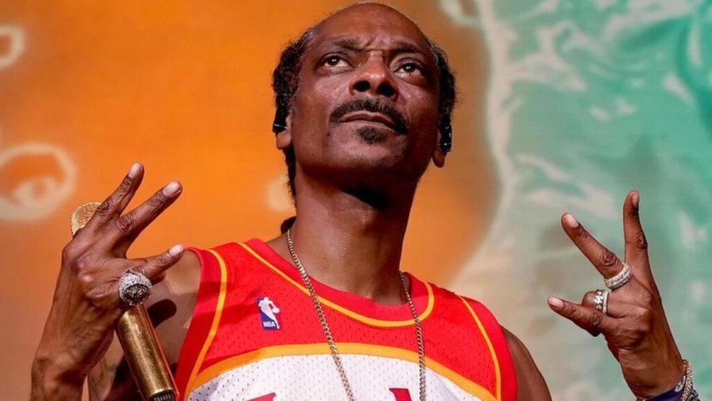 Snoop Dogg holding a microphone, wearing Hawkes jersey