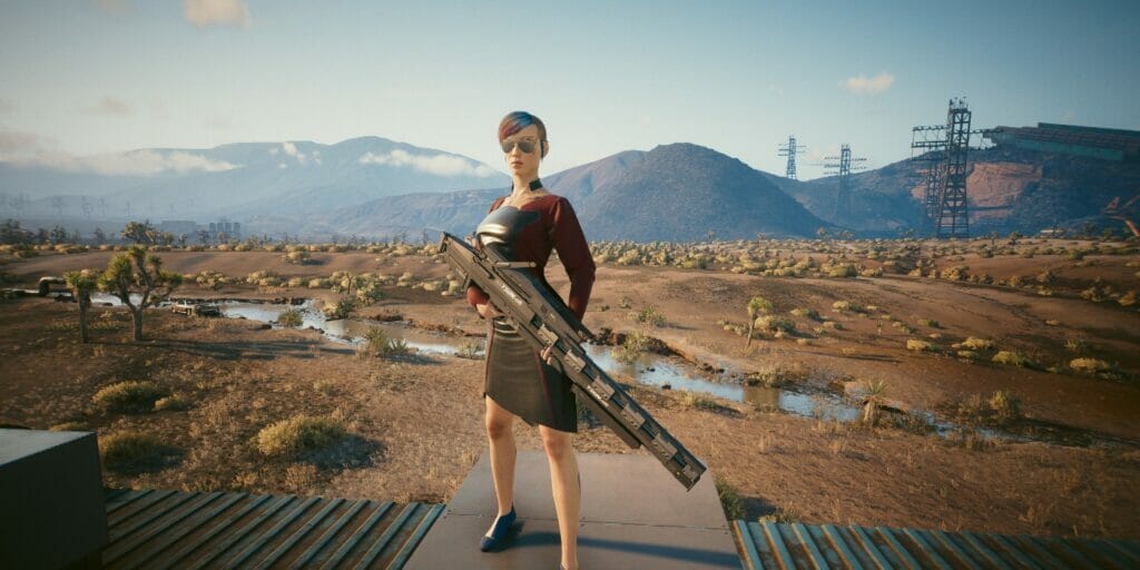 V stands with a sniper rifle in the desert in Cyberpunk 2077