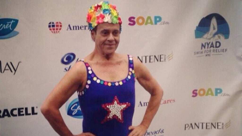 Richard Simmons in a colorful costume before a banner for SOAP and other advertisers