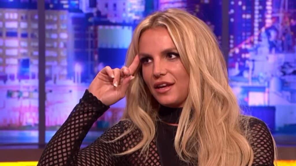 Britney Spears in a black dress gives an interview on a TV talk show.