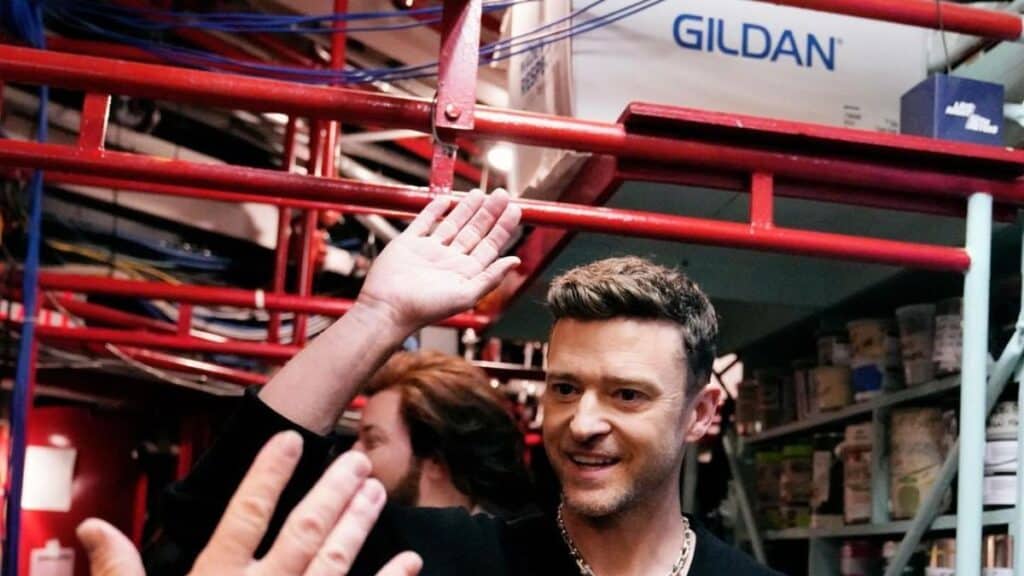 Justin Timberlake in a black outfit raises his hand