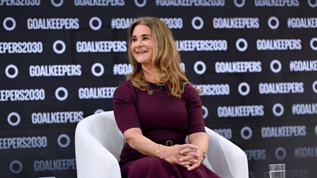 Melinda Gates in a burgundy dress seats on a chair