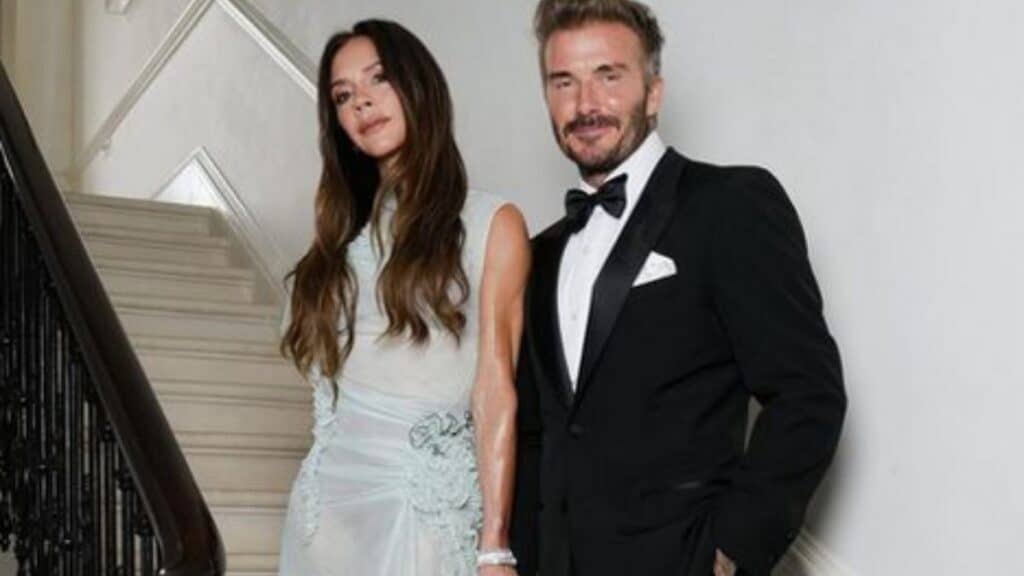 Victoria and David Beckham hold hands while posing together on a staircase.