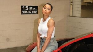 Blac Chyna in a white tank top and jeans sitting on a car